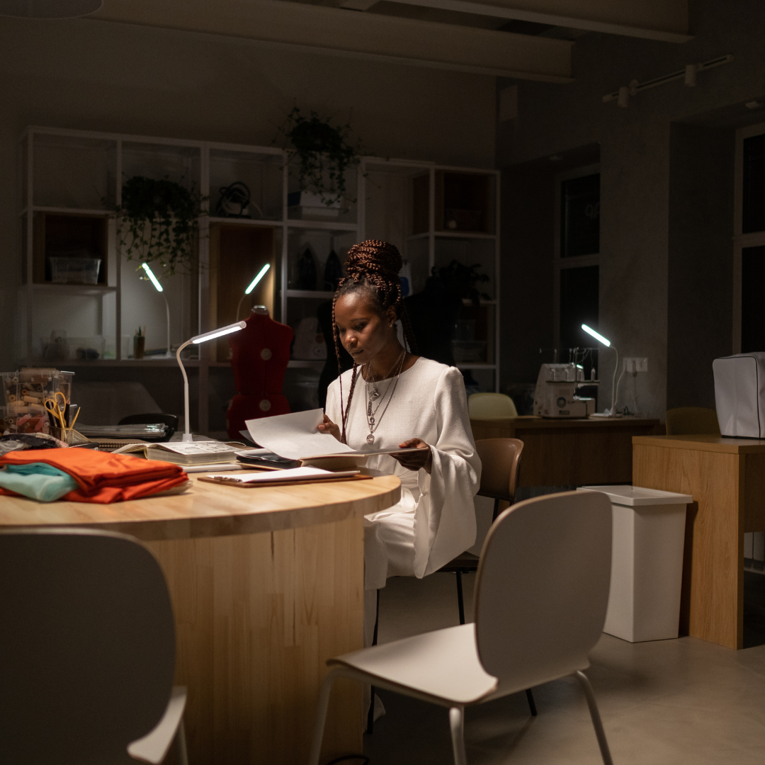 Woman sitting at a desk in a dimly lit office space, surrounded by books and papers.